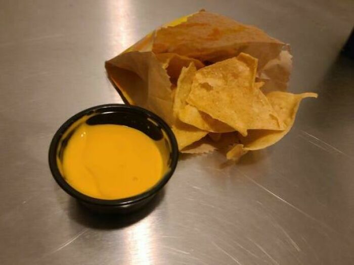 Small serving of nacho cheese dip with few tortilla chips in a paper bag, showing obvious shrinkflation in America.