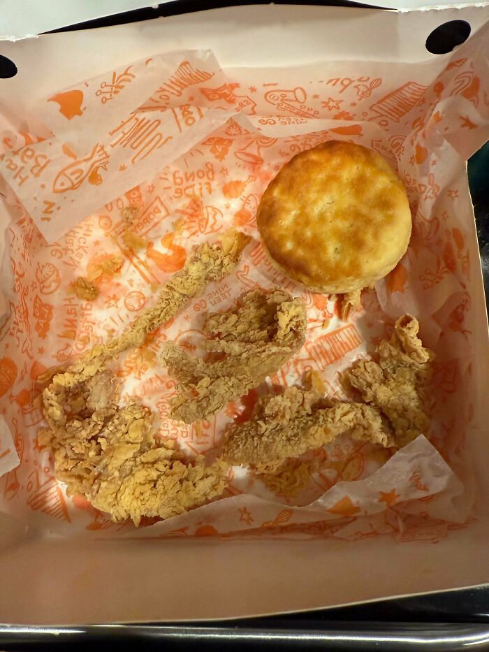 Shrunken fried chicken strips and a biscuit in a fast food box highlighting obvious shrinkflation in America.