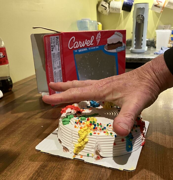 Hand pressing a noticeably smaller ice cream cake on a kitchen counter illustrating obvious shrinkflation effect.