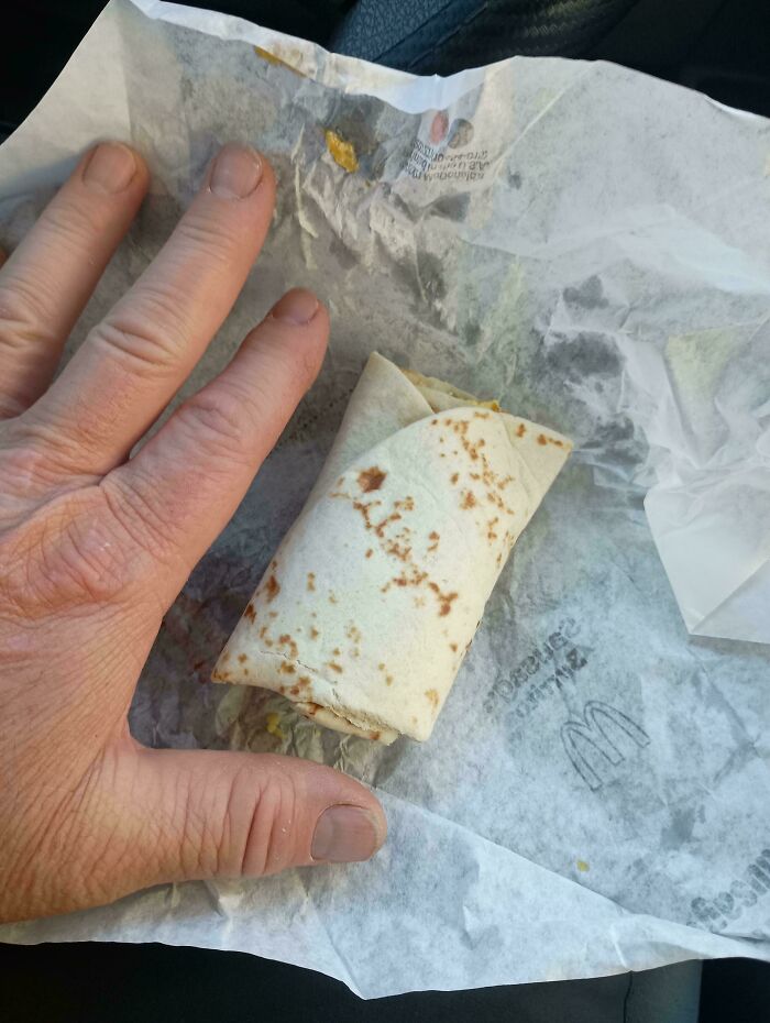 Hand next to a small fast food burrito on wrapper showing obvious shrinkflation in America food portions.