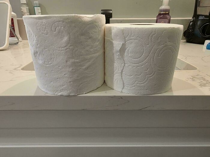 Two toilet paper rolls side by side showing shrinkflation with one roll visibly smaller than the other on a bathroom counter.
