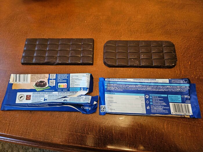 Two chocolate bars with packaging showing obvious shrinkflation comparison on a wooden table surface.
