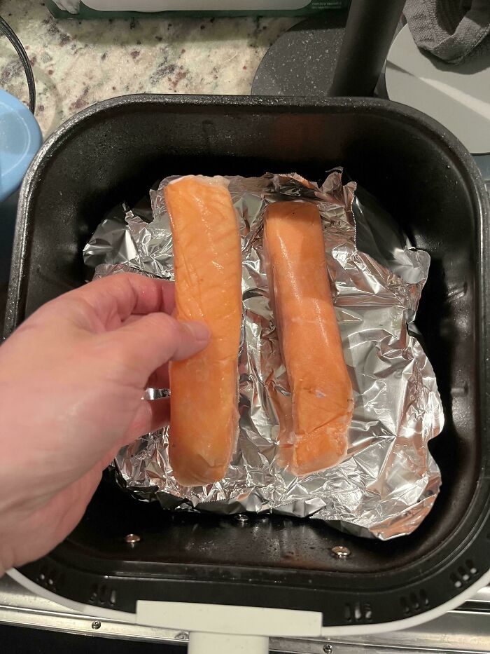 Hand holding smaller salmon fillet next to larger one in a tray, illustrating obvious shrinkflation in food product size.