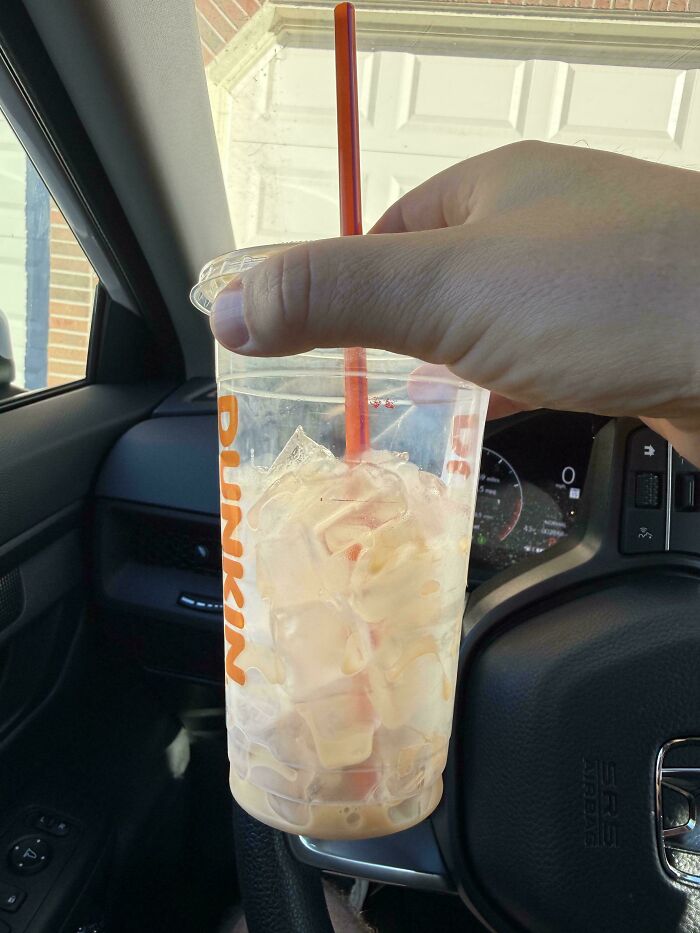 Hand holding a nearly empty Dunkin iced coffee cup with ice inside, illustrating obvious shrinkflation in America.