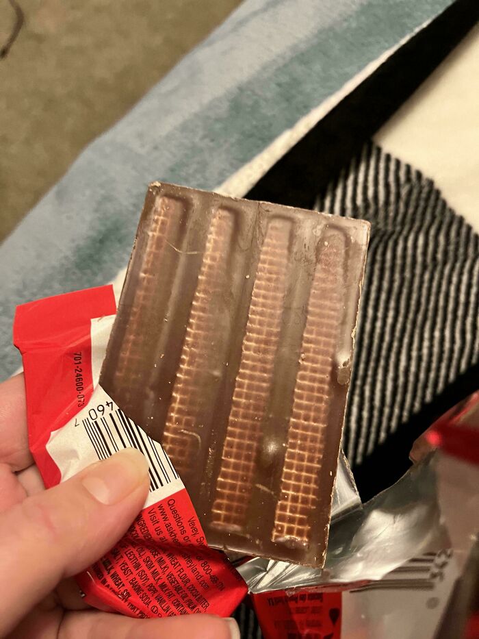 Partially unwrapped thin wafer chocolate bar held in hand, illustrating obvious shrinkflation in product size.