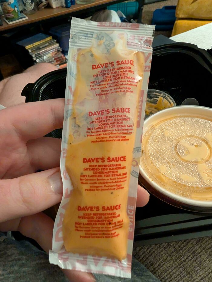 Hand holding a small packet of Dave’s Sauce next to a dipping cup, highlighting obvious shrinkflation in product packaging.
