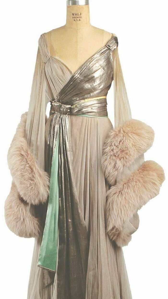 Elegant historical garment with metallic sash and fur-trimmed sleeves displayed on vintage dress form.