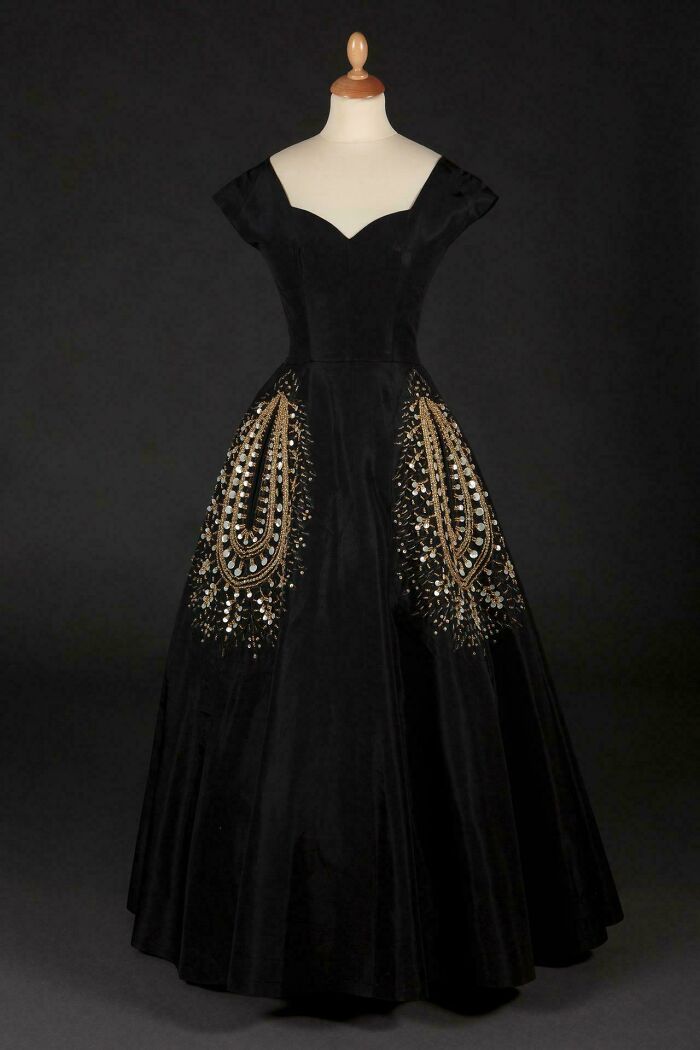 Black historical garment with gold and silver sequin embroidery displayed on a mannequin against a dark background.