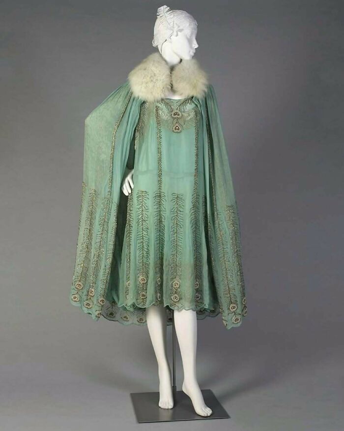 Mannequin dressed in a vintage historical garment featuring a green embroidered dress with a fur collar cape.