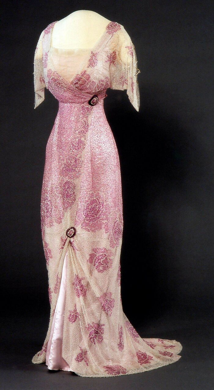 Early 20th century historical garment, elegant pink beaded dress with floral patterns and decorative brooches on display.