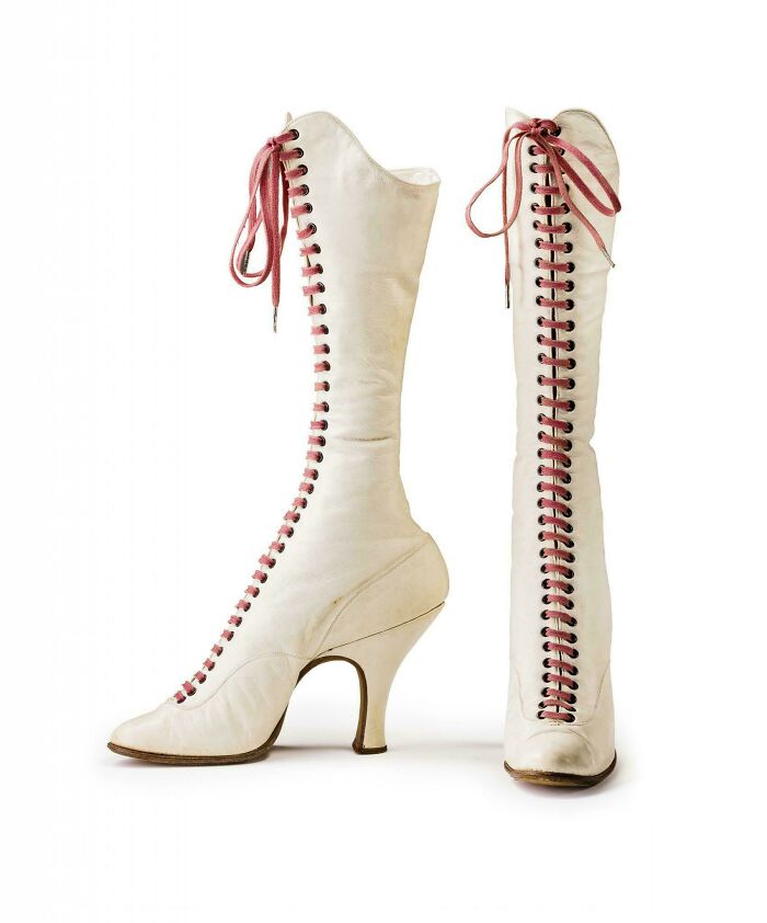 Pair of vintage white leather historical garments lace-up high-heeled boots with pink laces displayed on white background.