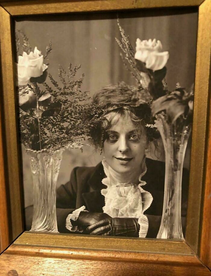 Vintage black and white photo of a woman wearing gloves and lace, framed with roses and ferns, reflecting historic photos.