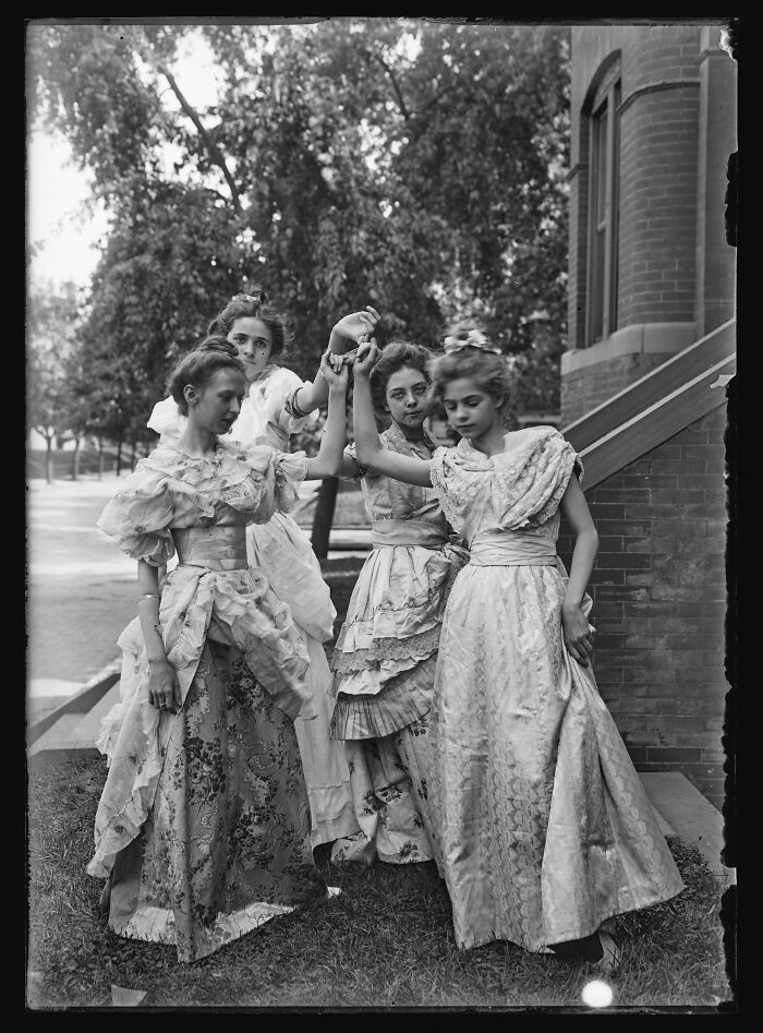 Four young women in vintage dresses pose outdoors, capturing a moment from decades ago with historic fashion and style.