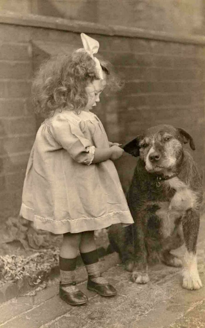 Vintage photo of a young girl gently interacting with a dog, capturing moments from decades ago with lasting emotion.