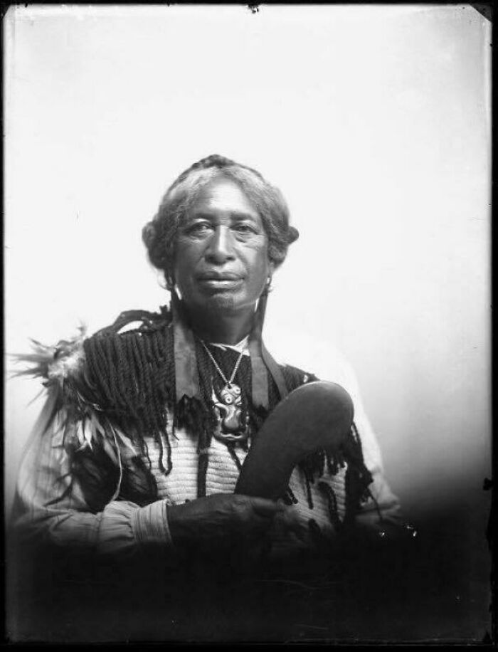 Black and white photo of a Native American man in traditional clothing holding a ceremonial object from decades ago.