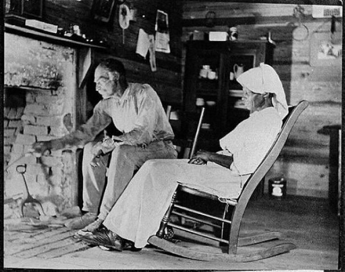 Black and white photo from decades ago of two people sitting by a fireplace, reflecting on simpler times and history.