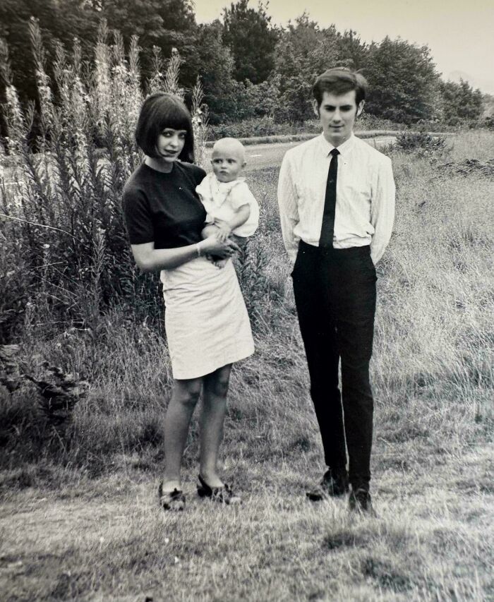 Black and white photo of a young family in vintage clothing standing outdoors decades ago, capturing timeless moments.