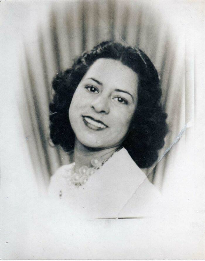 Black and white portrait photo from decades ago showing a smiling woman with curly hair and a pearl necklace.