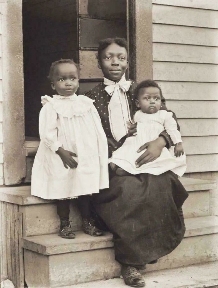 Vintage photo of a woman and two children on a wooden porch, capturing moments from decades ago.