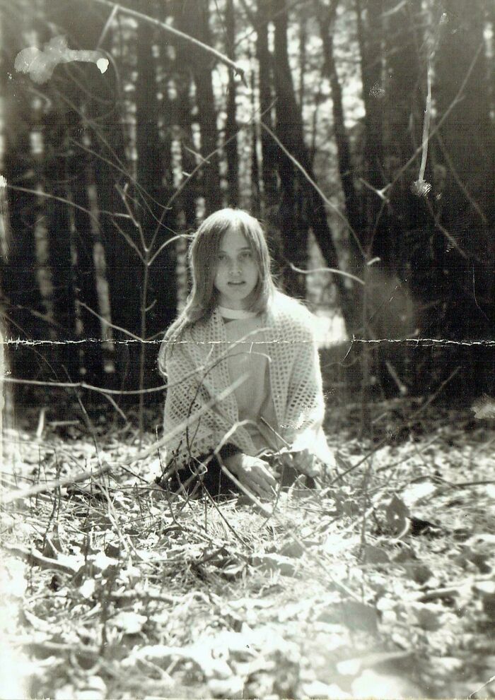 Black and white photo of a young woman sitting in the woods, vintage image symbolizing photos from decades ago.
