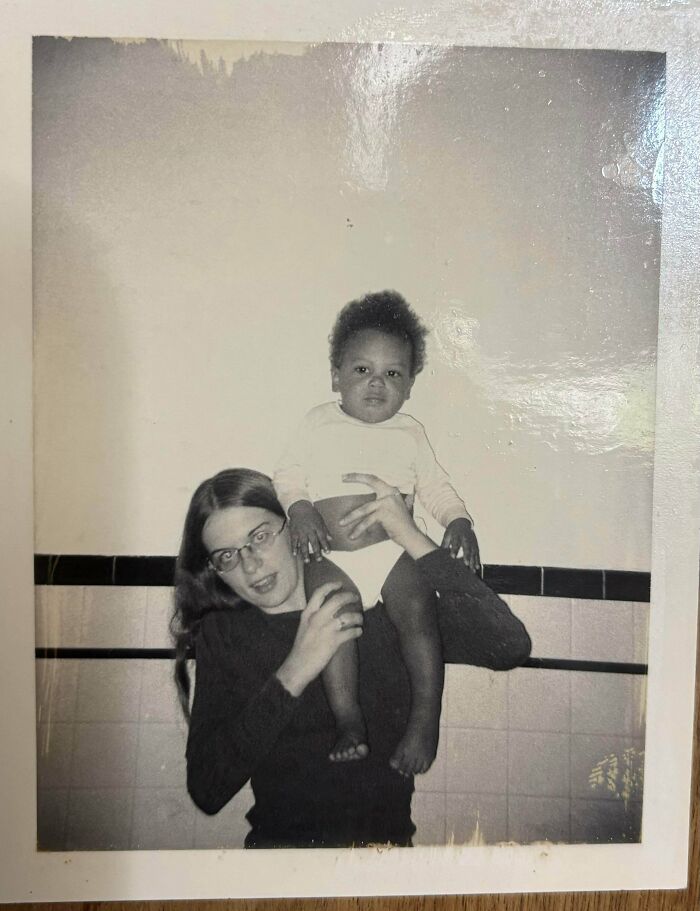 Black and white vintage photo of a woman with glasses holding a child on her shoulders, capturing moments from decades ago.