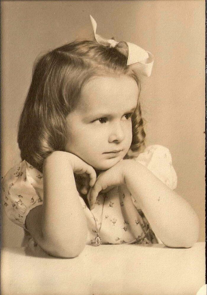 Vintage photo of a young girl from decades ago wearing a bow and floral dress, reflecting timeless moments from the past.