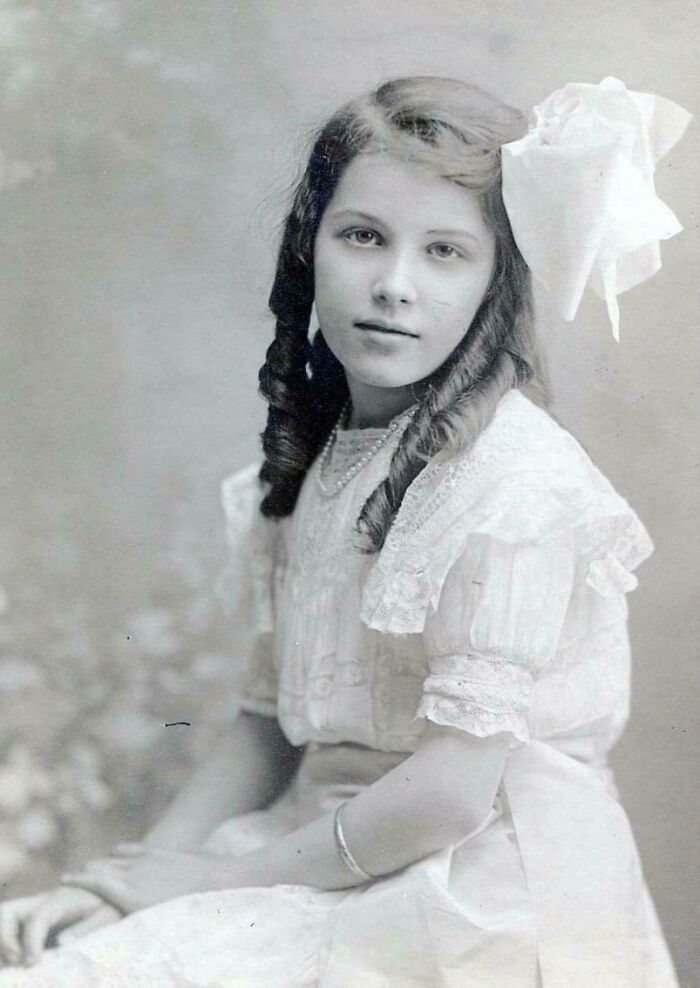 Black and white vintage photo of a young girl in a white dress with curls and a large bow from decades ago.