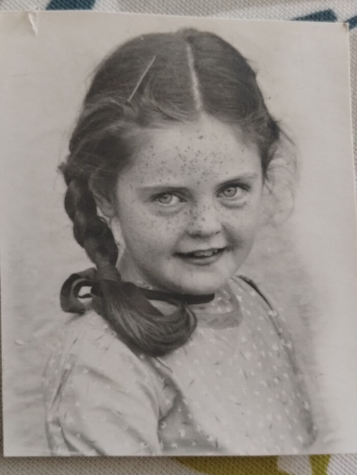 Black and white photo of a freckled young girl with braided hair, a vintage portrait reflecting decades ago moments.
