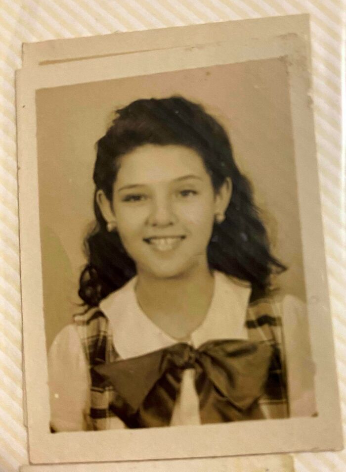 Vintage black and white portrait of a smiling young girl with wavy hair wearing a bow, from decades ago photos collection.