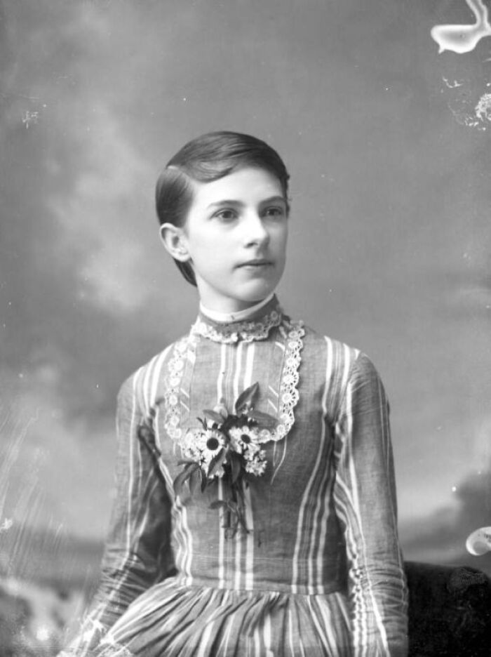 Black and white vintage photo of a young woman in a striped dress with floral decoration from decades ago.