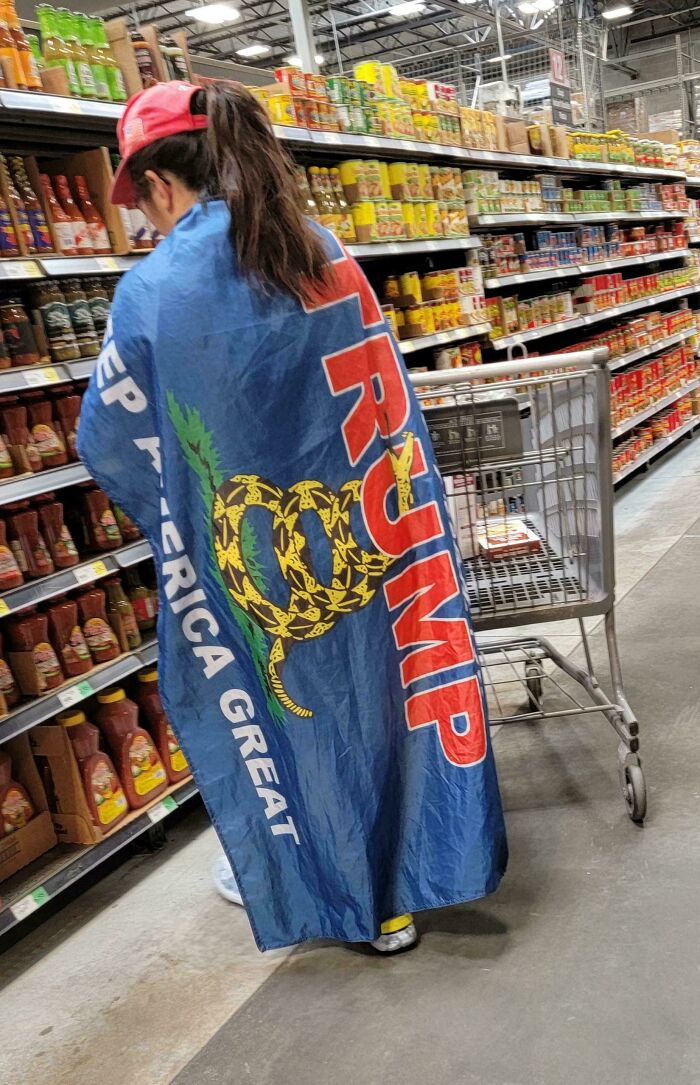 A person in a grocery store wearing a Keep America Great Trump flag as a cape, a cringey people example.