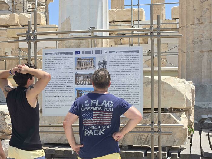 Two cringey men looking at a historical sign. One wears a shirt saying, IF THIS FLAG OFFENDS YOU, ILL HELP YOU PACK.