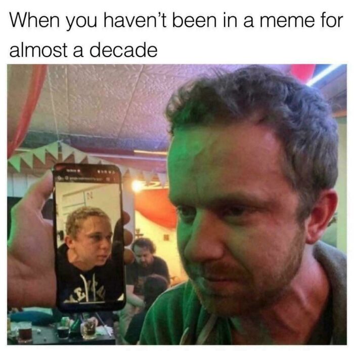 Man looking emotional while holding a phone showing an older meme face, illustrating favorite internet moments better than news.
