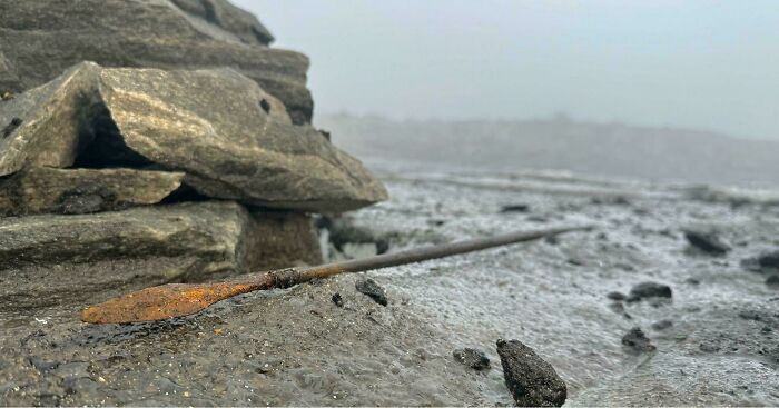 Rusty ancient spear artefact lying on mud near a pile of rocks, showcasing historical artefacts that survived to this day.