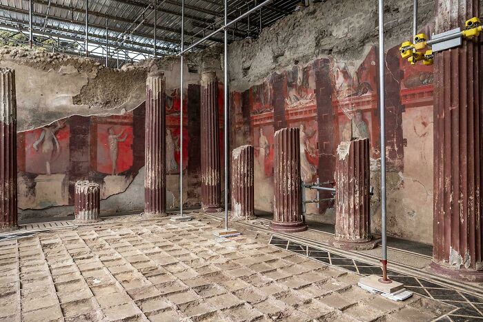 Ancient artefacts including weathered columns and murals preserved inside a historic archaeological site with protective roofing.