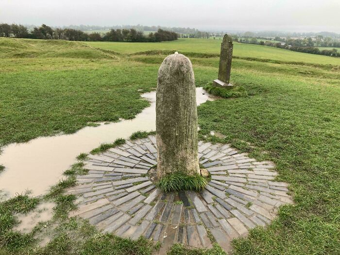 Ancient stone artefact surrounded by circular brickwork on a grassy landscape, symbolizing historical artefacts that survived.