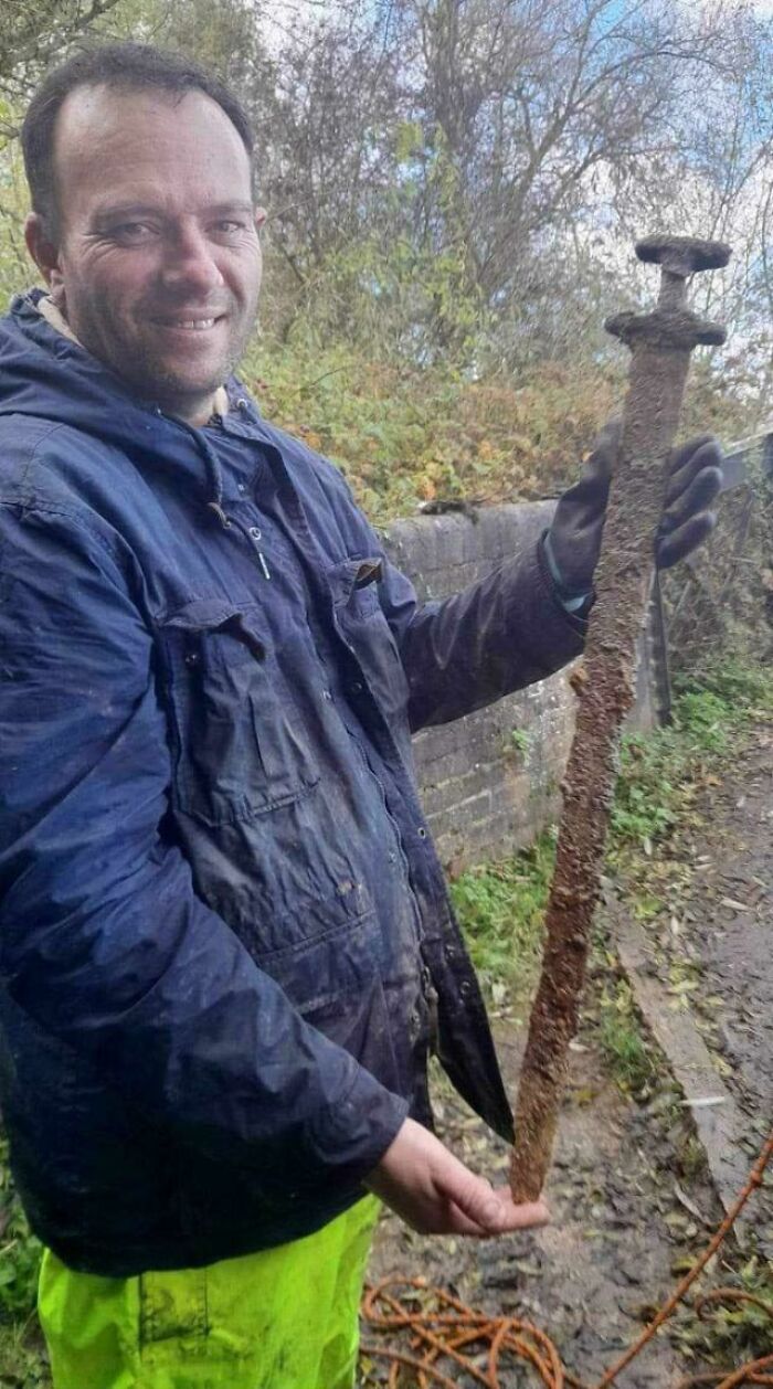 Man wearing blue jacket holding a rusted ancient sword, one of the fascinating artefacts that survived to this day outdoors.