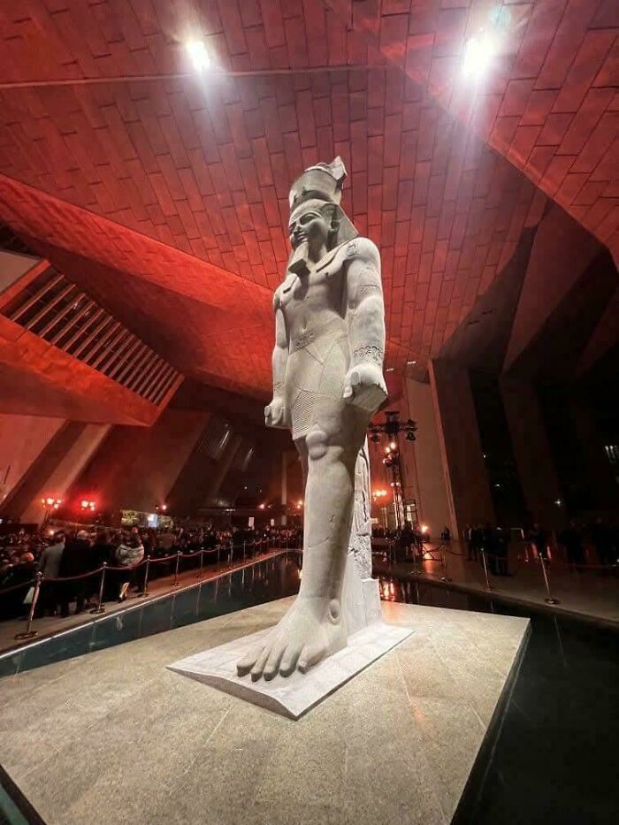 Ancient Egyptian statue illuminated in museum hall with visitors viewing this fascinating artefact of history.