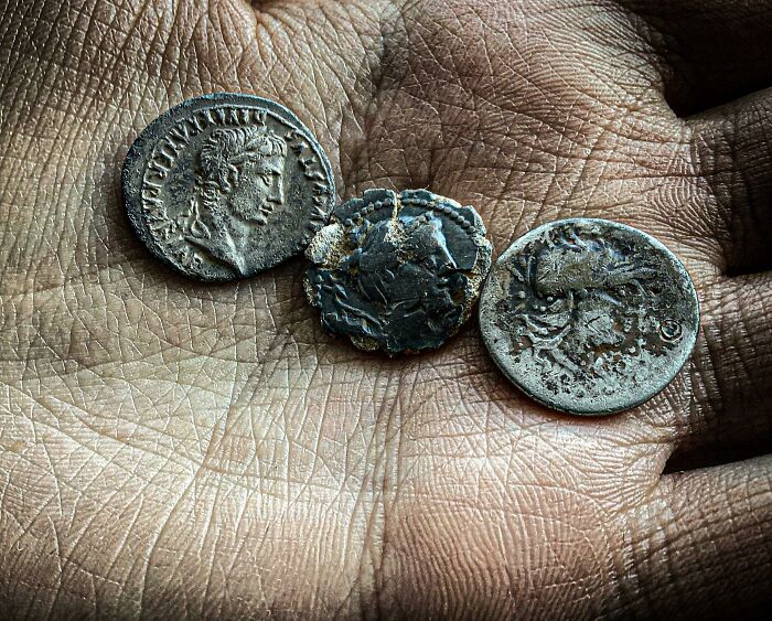 Three ancient artefacts in the shape of old coins resting on a person's palm, showing historical symbolism and details.