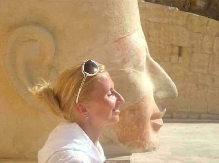 Woman smiling next to a large ancient stone head sculpture, showcasing fascinating artefacts that provide perspective on humanity.