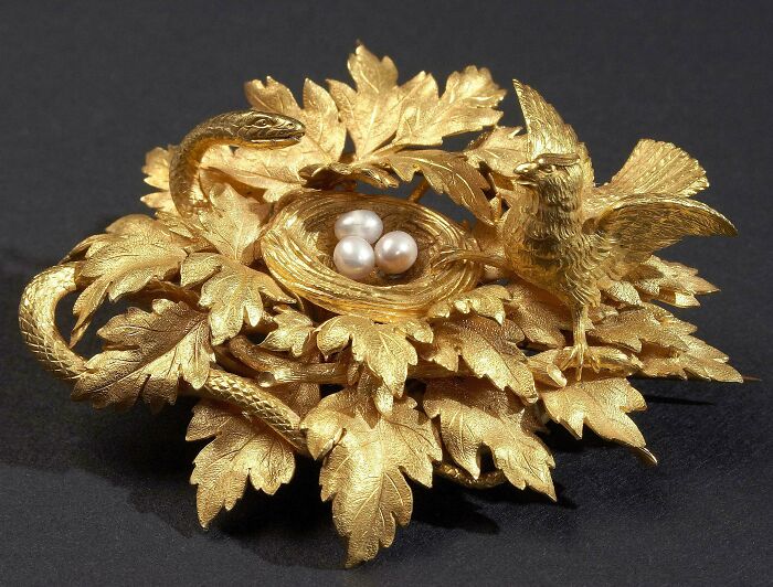 Intricate gold artefact featuring a bird, snake, leaves, and pearls, showcasing detailed craftsmanship and historical significance.
