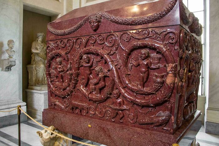 Intricately carved ancient red marble sarcophagus displayed indoors as a fascinating artefact of human history.