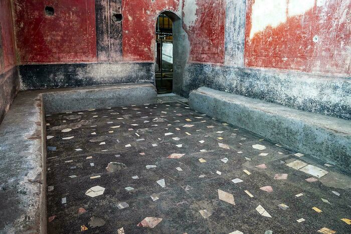 Ancient room with preserved mosaic floor and red plaster walls, showcasing artefacts that survived through history.