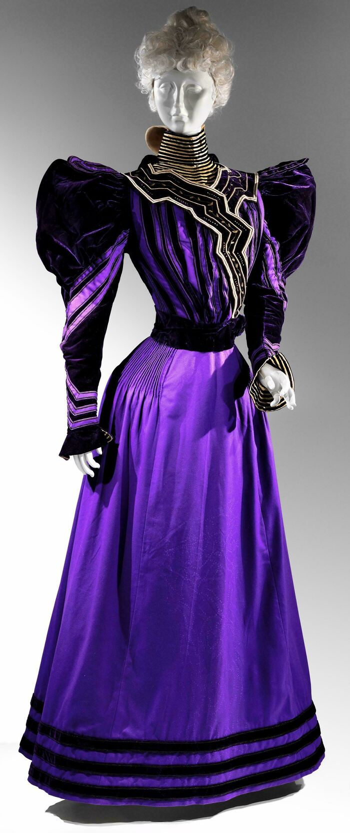 Victorian era purple silk dress with puffed sleeves, pleated skirt, and striped decorative trim historic artefact.
