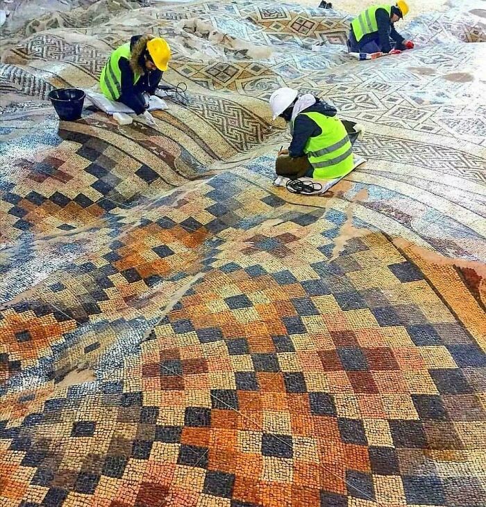 Archaeologists restoring an ancient mosaic artefact featuring geometric patterns, showcasing historical preservation efforts.