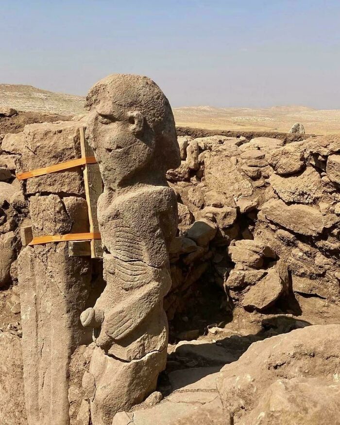 Ancient stone statue with detailed human features standing among archaeological ruins on strange Earth landscape.