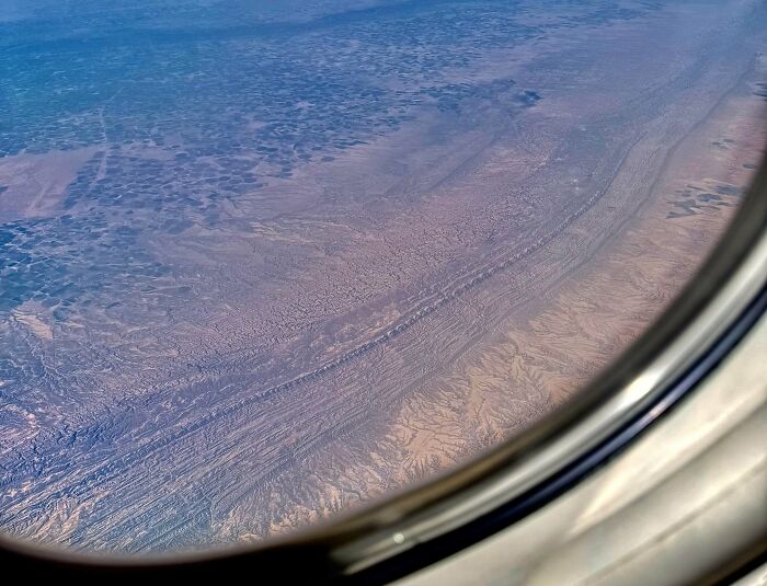 Aerial view of a strange earth landscape with unusual geological formations seen through an airplane window.