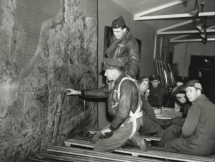 Historical photo of soldiers in leather jackets studying a large map inside a dimly lit room during wartime planning.
