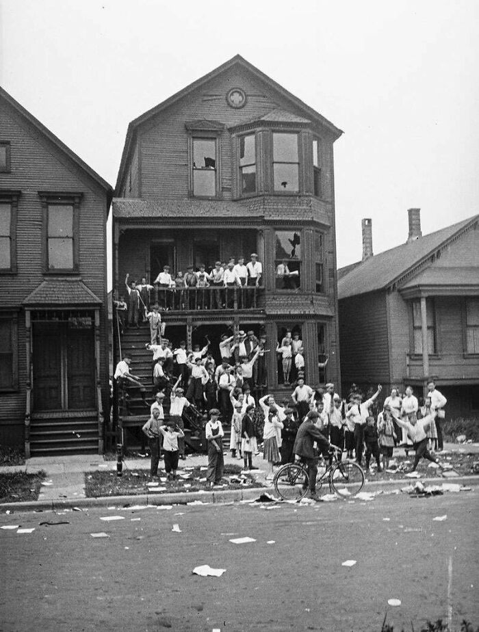 Group of people gathered outside an old house in a historical photo representing a vastly different world.
