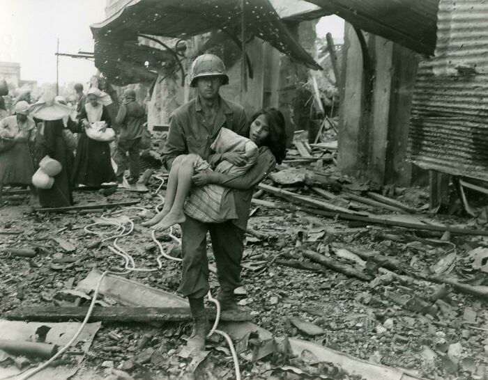Historical photo of a soldier carrying a child through war-torn rubble in a vastly different world from today.